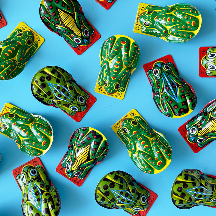 Several green tin frog clicker toys arranged on a light blue background.