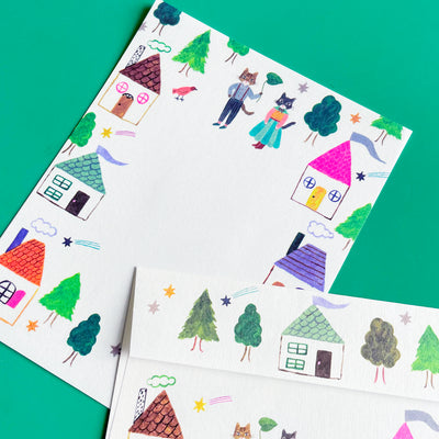 A close-up photo of the writing paper that features two anthropomorphic cats in outfits and colorful houses around the border.