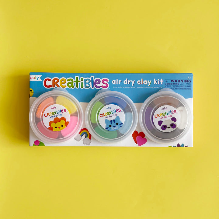 Three containers of multi colored clay in one package on a yellow background.