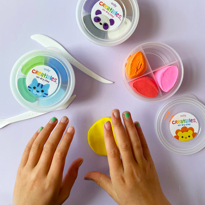 Three containers of multi colored clay. A child's hands plays with yellow clay in the foreground.