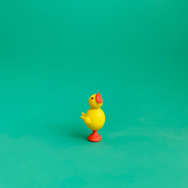 A small wooden chick figurine on a green background.