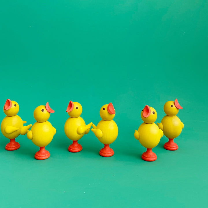Six small wooden chick figurines on a green background.