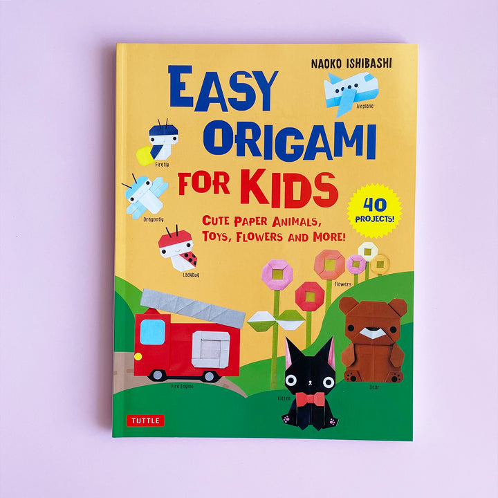 Easy Origami for Kids book displayed on a pink background. Book cover features origami projects including a cat, bear, fire truck and bugs.