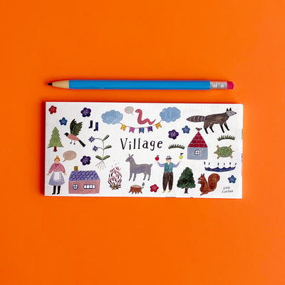 The Village memo pad sits on an orange background next to a pencil for scale. It's about the same length as the pencil.