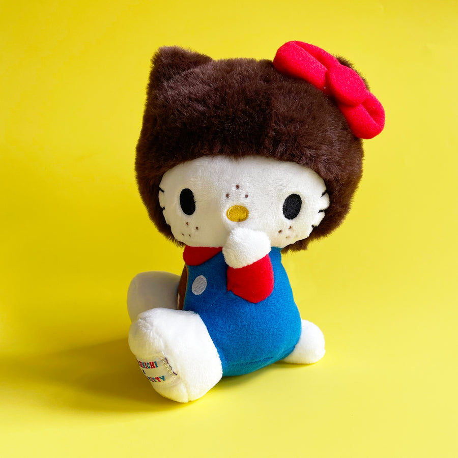 Plush toy resembling Hello Kitty wearing a brown hat with a red bow on a yellow background.
