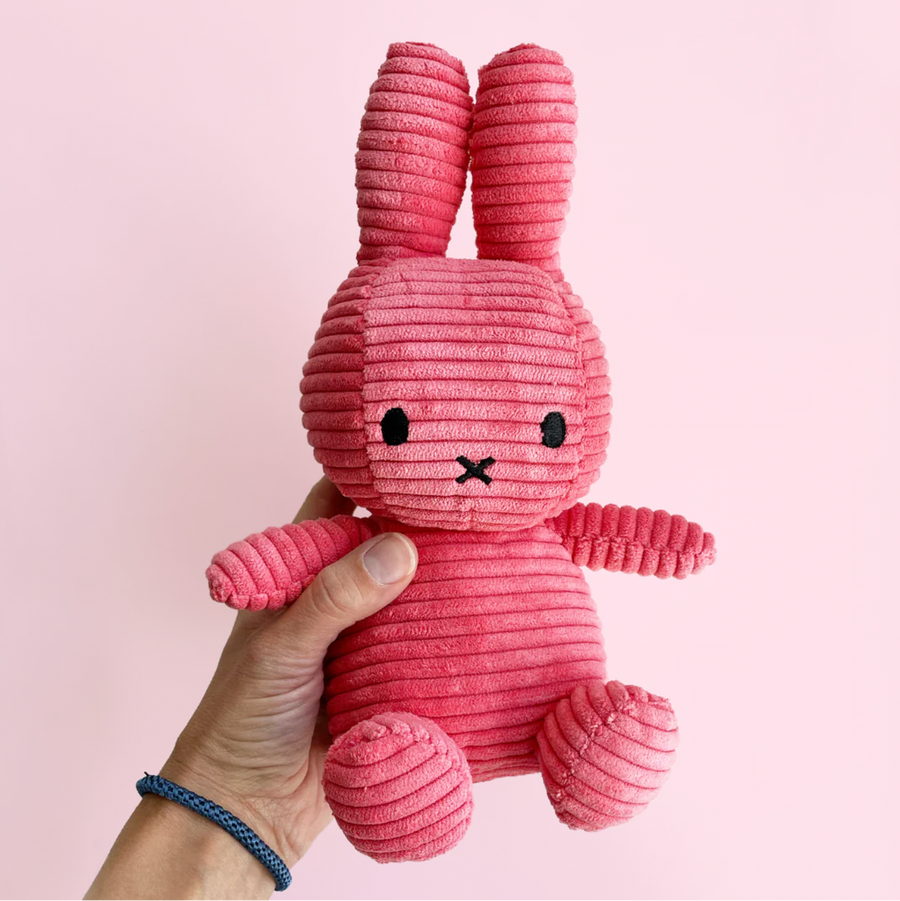 Pink corduroy bunny toy held by a hand against a pink background