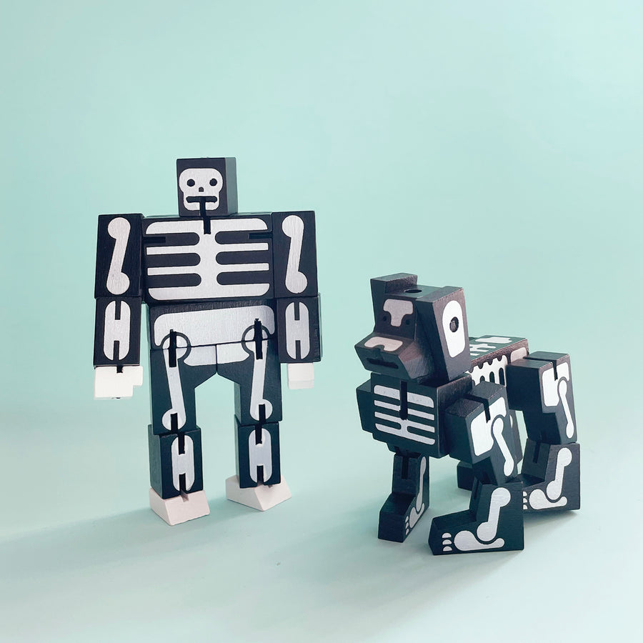 Skeleton themed wooden folding toys standing up next to each other. One is in the shape of a human, the other a dog. 