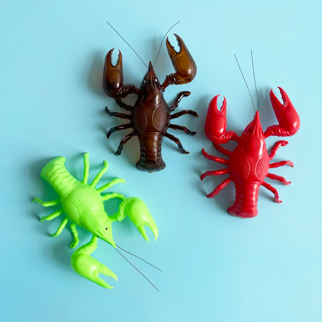 Three lobster shaped bobblehead figurines in neon green, brown, and red. 