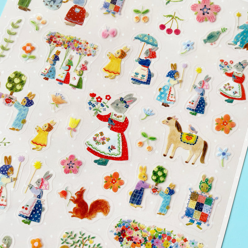 A close up of the Rabbits sticker sheet, showing a sticker of a grey rabbit in a red dress with a floral apron, holding a bouquet of flowers. A red squirrel holding a flower and a horse with a bird perched on its back are also featured.