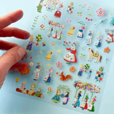A hand holds the translucent Rabbits sticker sheet over a blue background.
