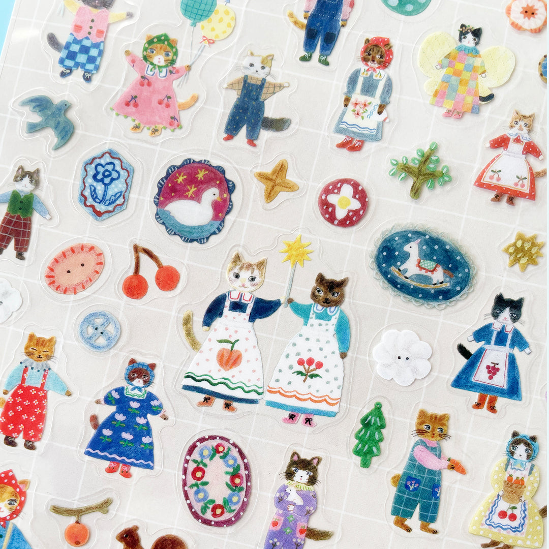 A close up of the Cats sticker sheet, featuring stickers of buttons, a swan, a rocking horse, and two cats in blue dresses and floral aprons holding a magic wand together.