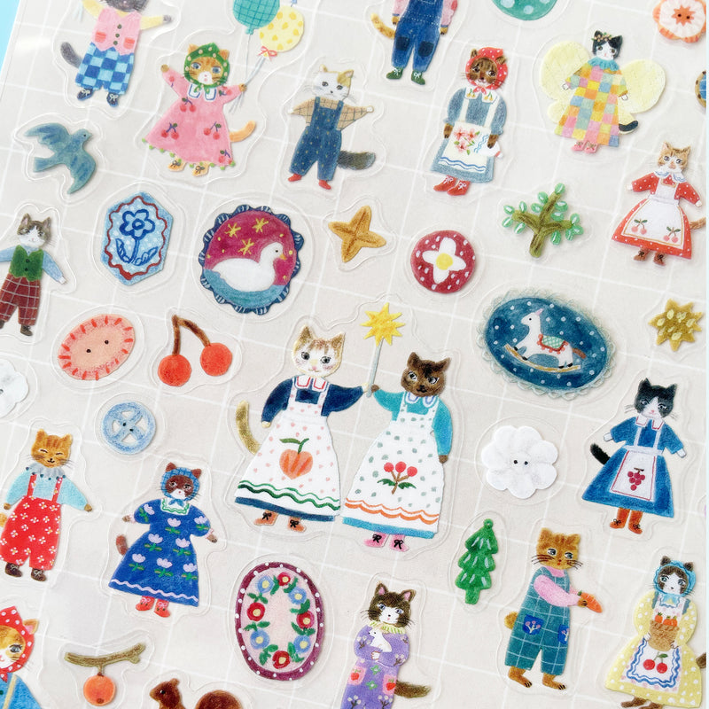 A close up of the Cats sticker sheet, featuring stickers of buttons, a swan, a rocking horse, and two cats in blue dresses and floral aprons holding a magic wand together.