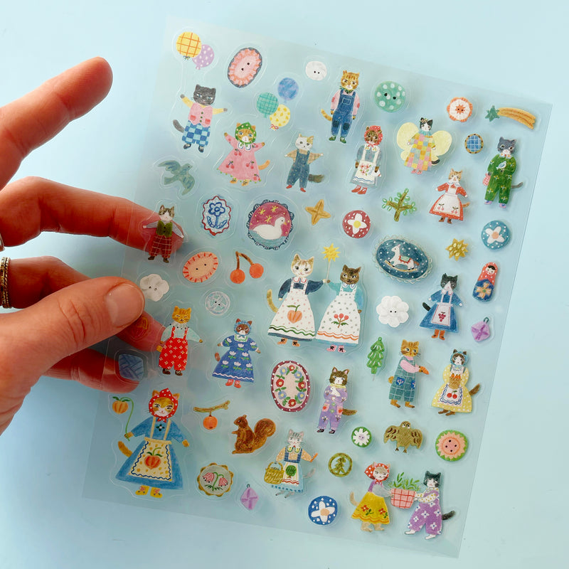 A hand holding the translucent Cats sticker sheet over a light blue background.