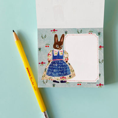 This page of the memo pad has a white writing area on a blue background with flowers and cherries. An anthropomorphic rabbit in a floral dress is illustrated next to the writing area.