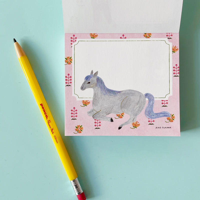 This page of the memo pad has a white writing area on a pink background with flowers and berries. A grey horse with a blue mane is illustrated under the writing area.