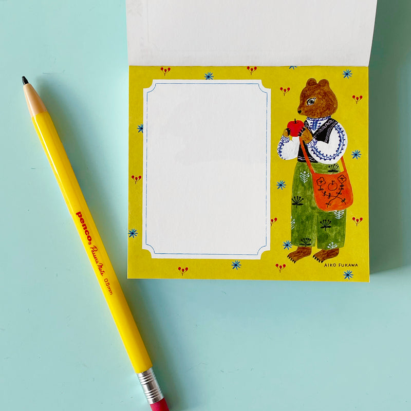 This page of the memo pad has a white writing area on a yellow background with blue flowers and berries. An anthropomorphic bear in a vest and green trousers is illustrated next to the writing area.