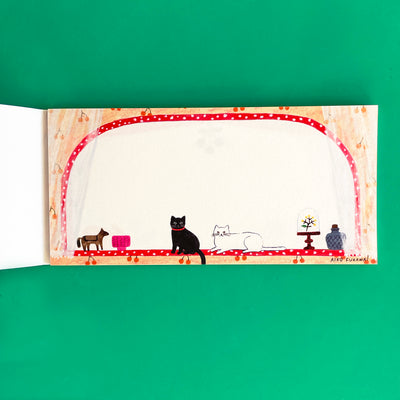 This page of the memo pad shows a black cat and a white cat on a red windowsill next to various trinkets. The window is surrounded by lace curtains and orange cherry wallpaper.
