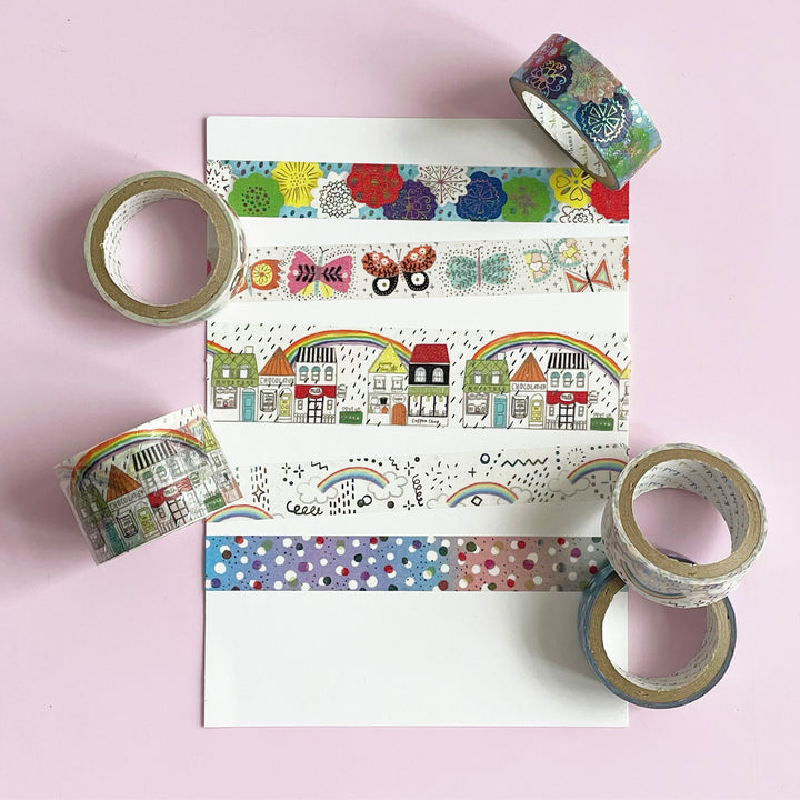 A white paper with stripes of colorful washi tape featuring sparkling designs of flowers, butterflies, rainstorms and dots. 