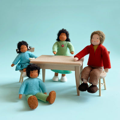 4 cotton dolls of various sizes sit around a light wooden table and chairs.