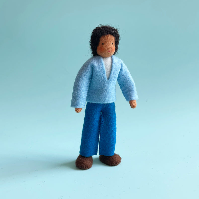 A 5.25-inch cotton doll with medium skin and dark curly hair wearing a light blue felt top and blue felt pants.