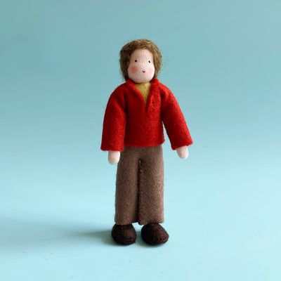 A 5.25-inch cotton doll with light skin and brown hair wearing a red felt top and brown felt pants.