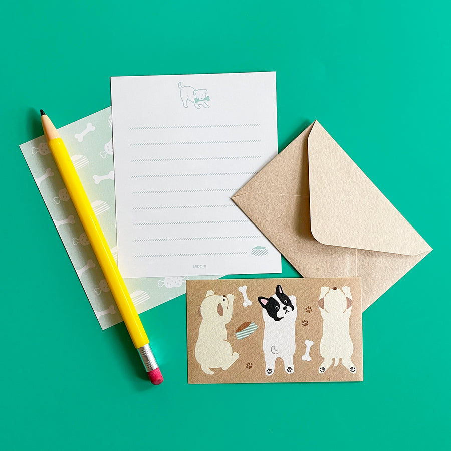 Letter writing set with a pencil, paper, envelope, and postcard featuring dog illustrations on a green background.