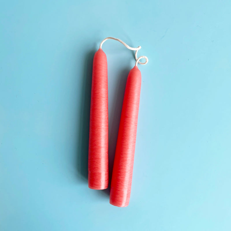 A pair of bright pink 6 inch taper candles connected by their wicks.