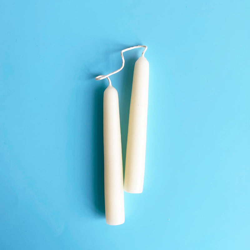 A pair of white 6 inch taper candles connected by their wicks.