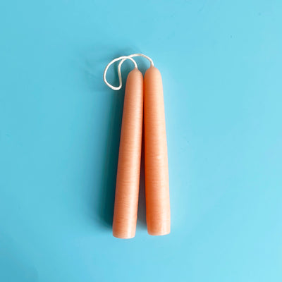 A pair of light peach 6 inch taper candles connected by their wicks.