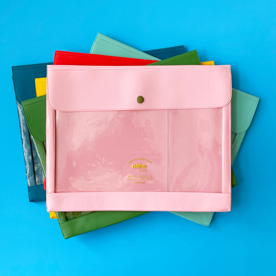 Stack of colorful plastic envelopes with a large clear window, with a pink envelope on the top of the stack. 