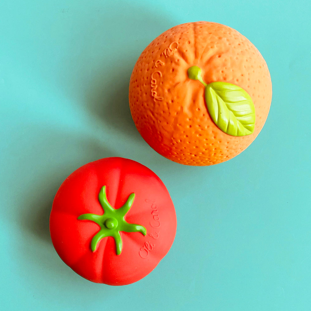 Two rubber balls that look like a ripe tomato and large ortange displayed against a bright green background. 