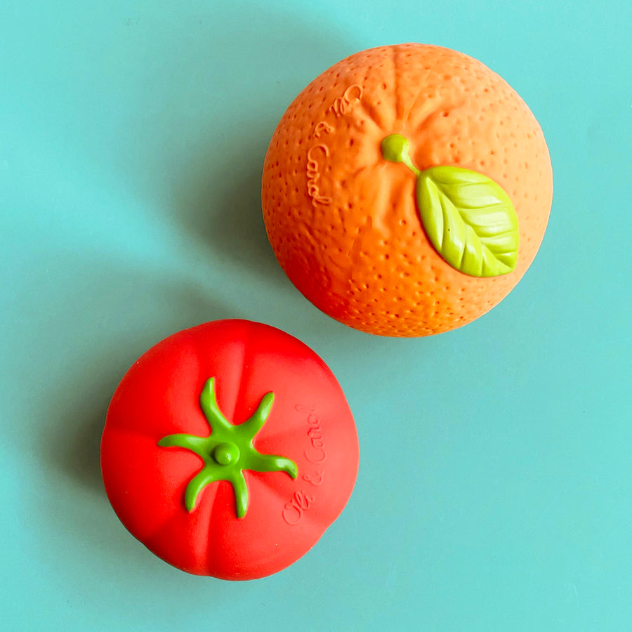 Two rubber balls that look like a ripe tomato and large ortange displayed against a bright green background. 