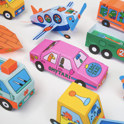 A close-up of the 3d paper vehicles, highlighting a pink paper car that has a cartoon bird sitting in the back seat and the words "Croc Taxi" on the hood.