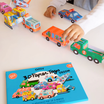 A child's hands play with the 3d paper vehicles, reaching for an orange bus with cartoon lizards
