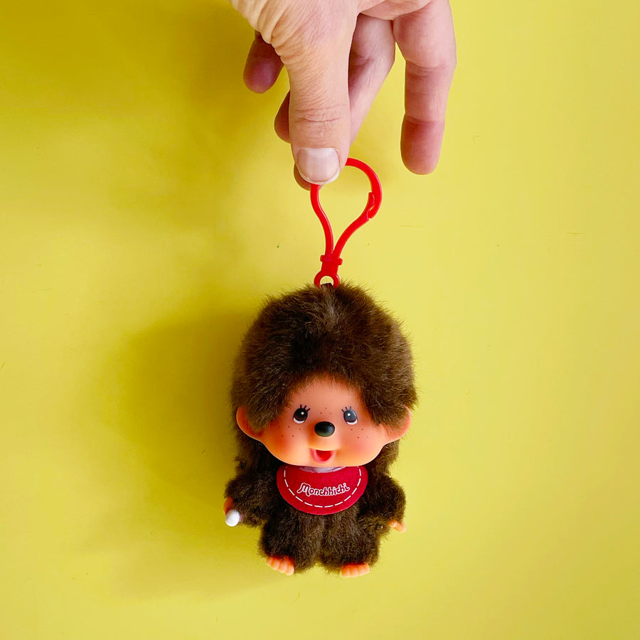 Monchhichi-shaped keychain with a red clip on a yellow background