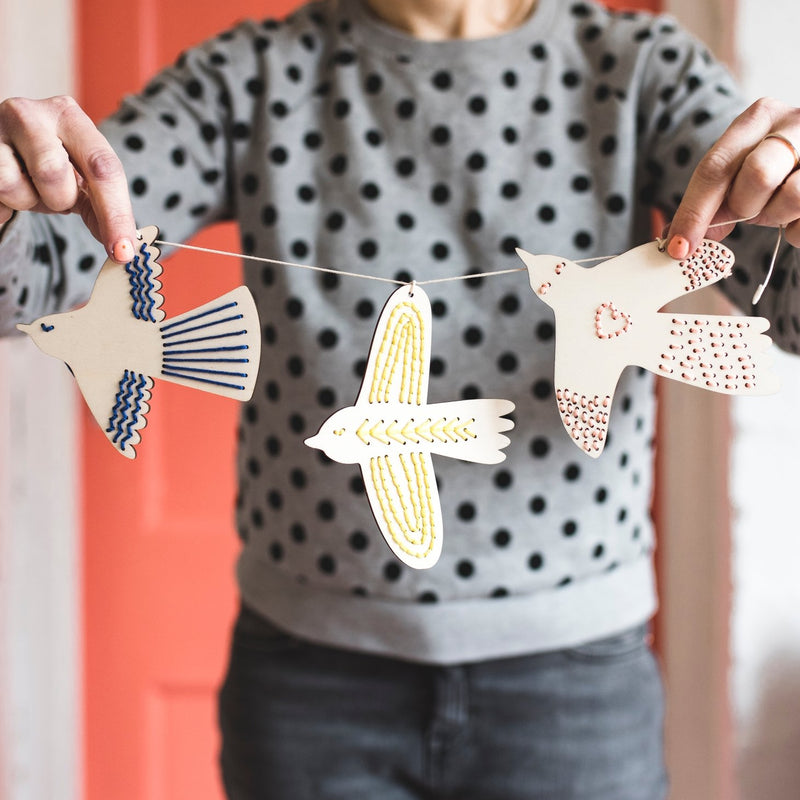 A garland of  three wooden birds with stitched details being held by a woman in a polka dot sweater.