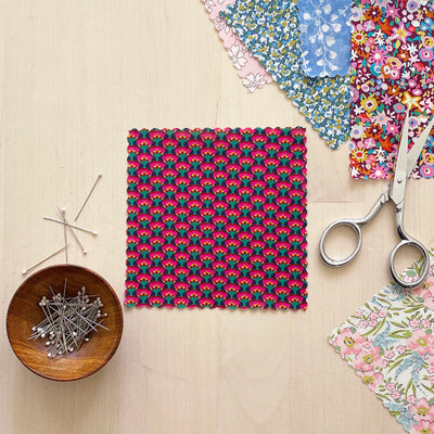 Square of printed fabric framed  by other fabrics, pins and scissors.