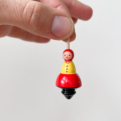 One small babushka lady top being held in a thumb and forefinger on a white background. 