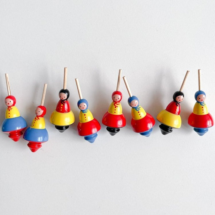 Eight small babushka lady shaped tops in a horizontal line on a white background.