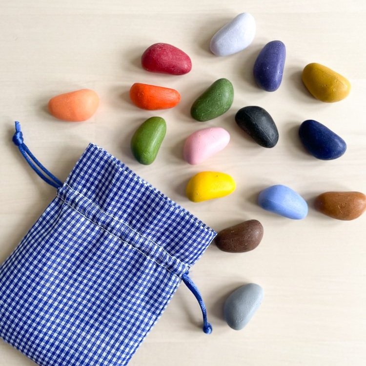 A small blue gingham bag open with several colorful crayon rocks  on a wooden background. 