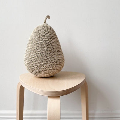Crocheted pear sitting on a stool in front of a white background. 