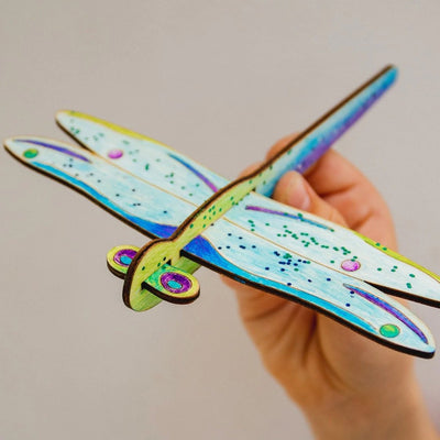 Wooden dragonfly glider being held by a child's hand. 
