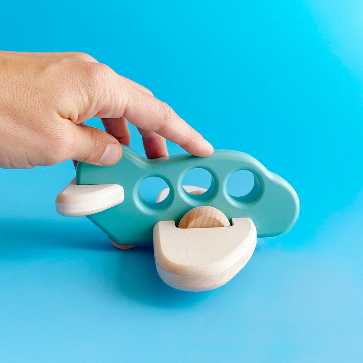 A hand holds the wooden airplane for scale over a blue background.