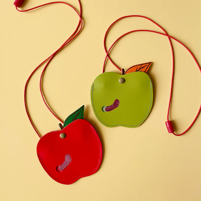 Two apple shaped purses, one red and one green, on a yellow background