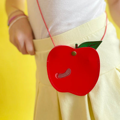 Red apple shaped purse being worn by a child in a yellow skirt