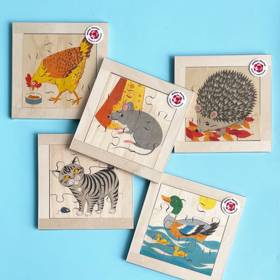 5 different light wood puzzles. The images are created by 9 puzzle pieces. Each puzzle depicts a chicken, a mouse with cheese, a hedgehog in autumn leaves, a cat with a mouse toy, or a duck on water with ducklings.