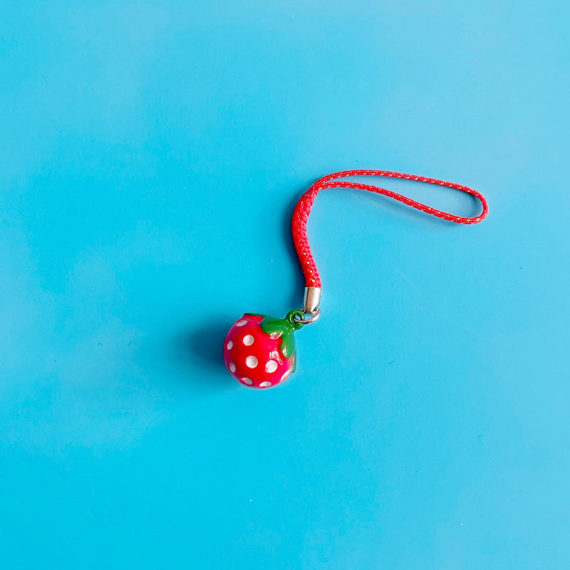 Small red strawberry shaped bell against a blue background.