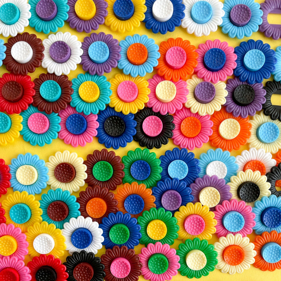 Several rows of multi colored plastic flower clips on a yellow background. 