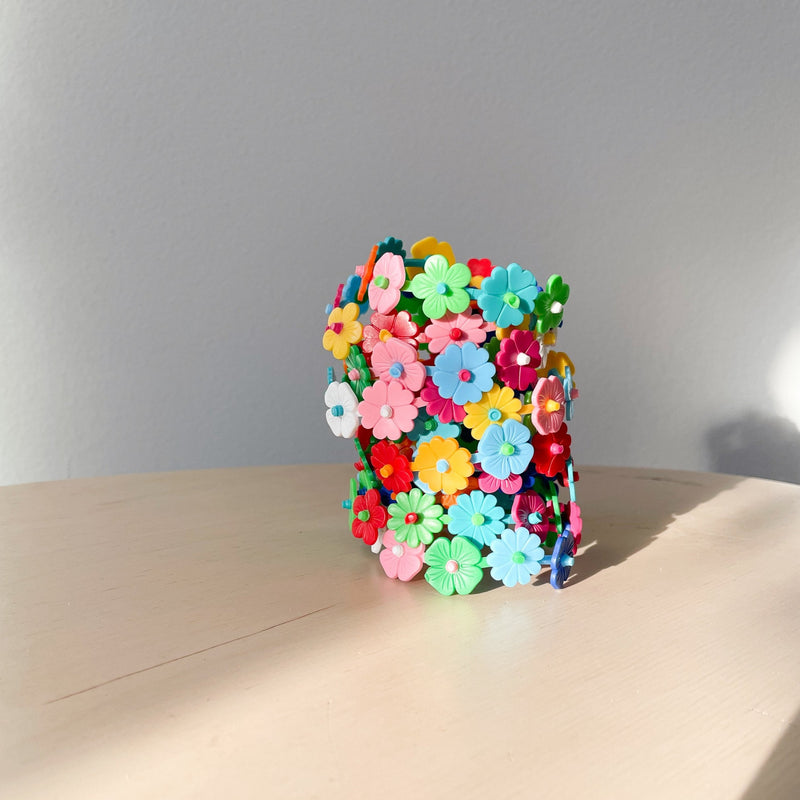 Colorful plastic flower clips assembled into bracelets stacked up on a wood table in front of a white background