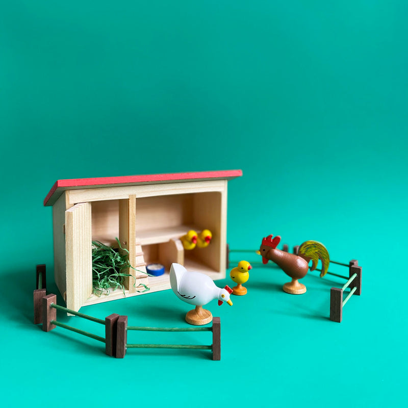 Wooden chicken coop with a hen, rooster and three chicks, on a green background.